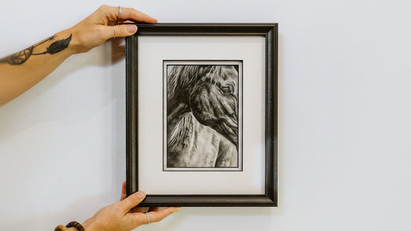 Person holding a framed black and white print against a white wall.