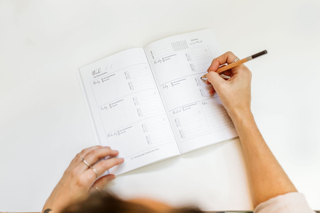 Person writing in a planner with a pencil on a white surface