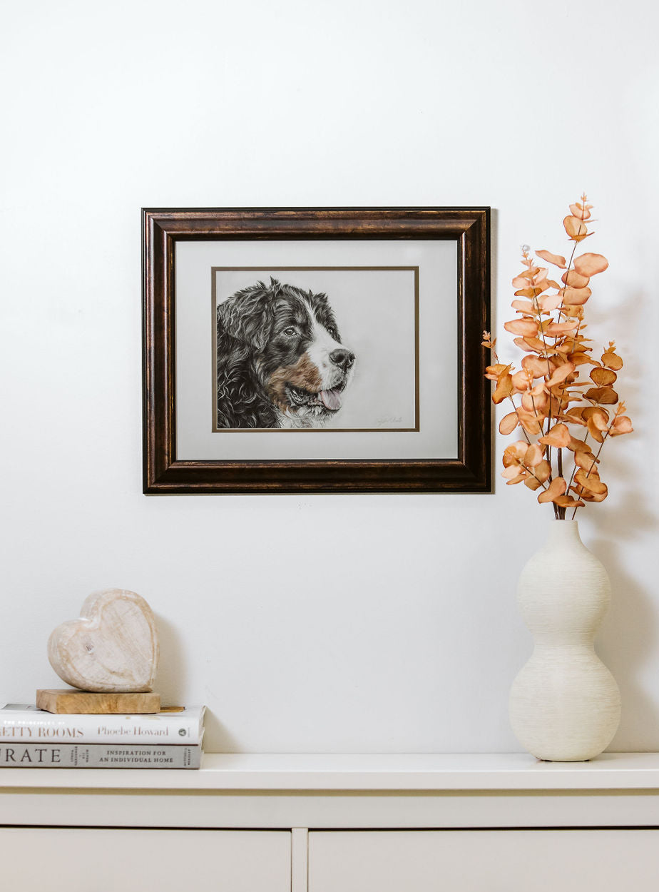 Framed artwork of a Bernese Mountain Dog on a wall above a white cabinet with decorative items.