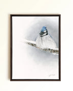 A framed pastel drawing of a blue jay perched on a snowy branch, set against a soft white and blue winter background. The artwork is presented in a dark brown wooden frame and hangs on a light beige wall.