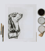 Pastel drawing of a dog on a white background with art supplies.