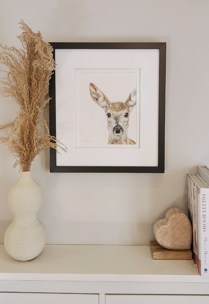Framed artwork of a deer on a shelf with decorative items.