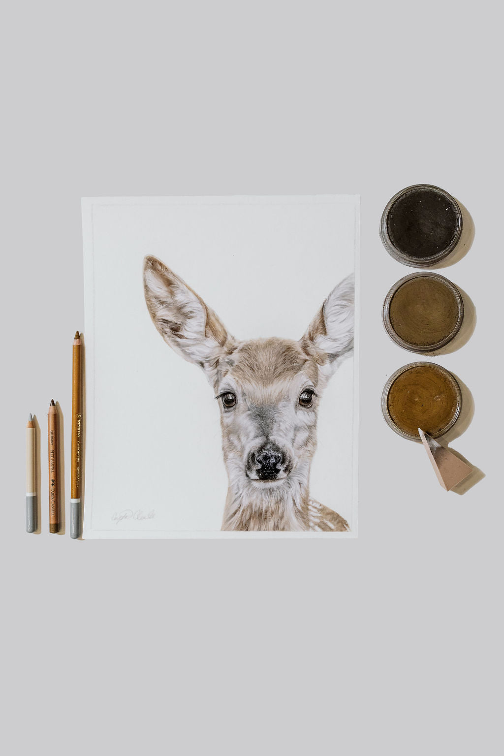 Artwork of a deer face with pastel supplies on a light gray background