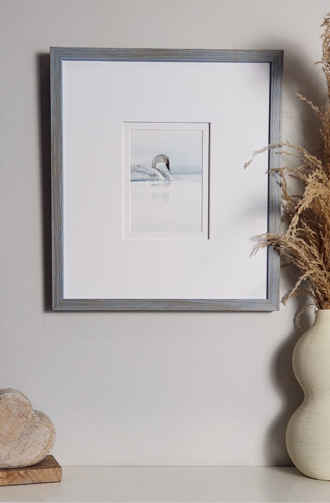 Framed artwork of a swan on a white wall with a vase and decorative object in the foreground.