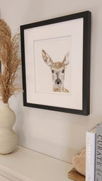 Framed artwork of a deer on a wall with decorative elements.