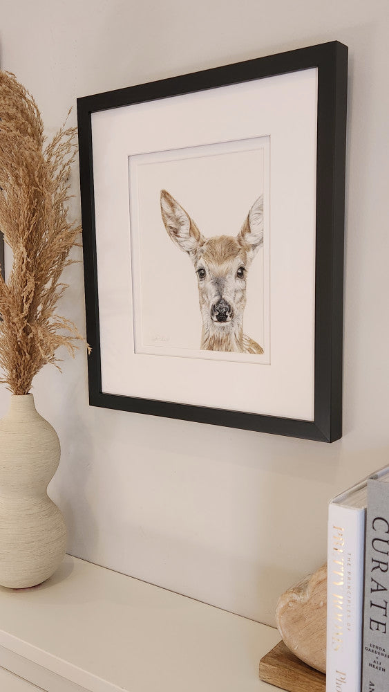 Framed artwork of a deer on a wall with decorative elements.