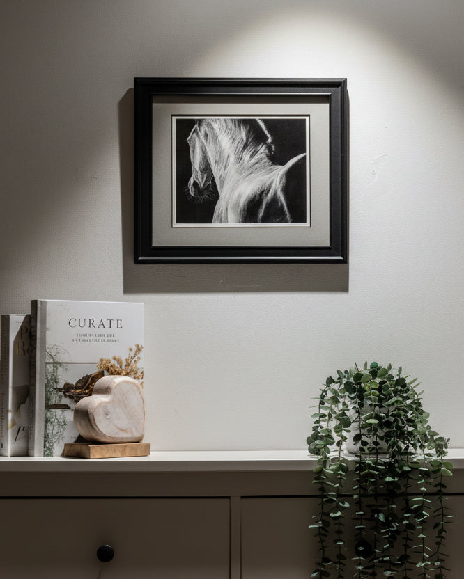 Framed black and white artwork on a wall above a white cabinet with decorative items.