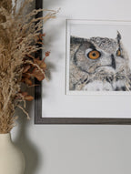 Framed owl artwork on a wall with decorative elements.