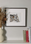 Framed picture of an owl on a shelf with books and a vase.