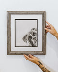 Person holding a framed black and white boxer dog drawing against a white wall