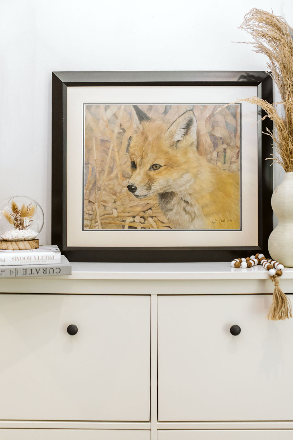 Framed artwork of a fox on a shelf with decorative items.