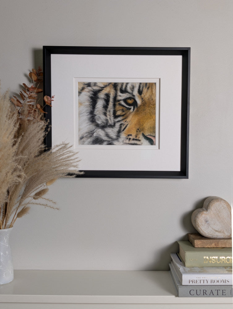 Framed artwork of a tiger's face on a shelf with decorative items.