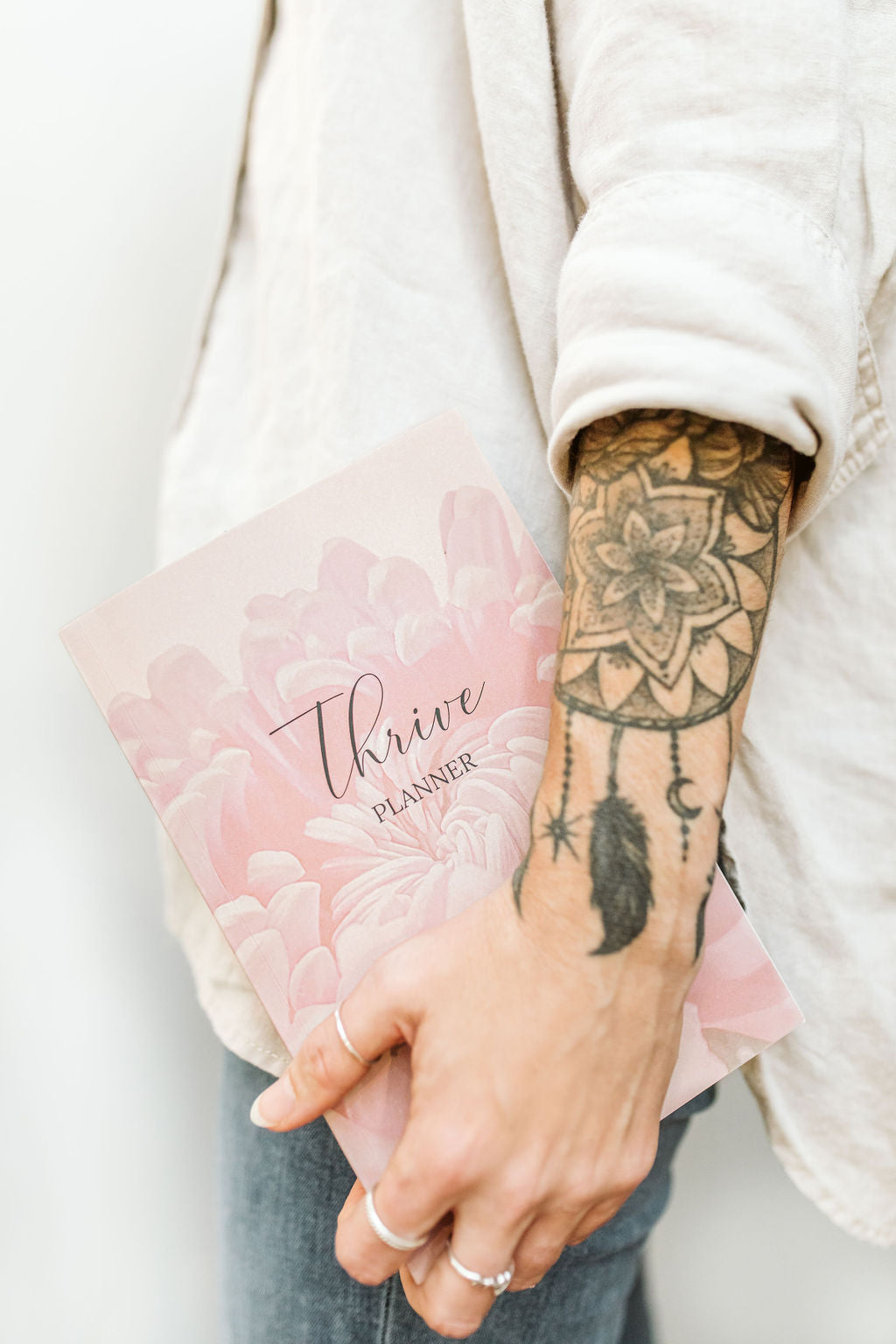 The artist, Crystal Clarke, holding a pink yearly planner with 'Thrive' branding, 