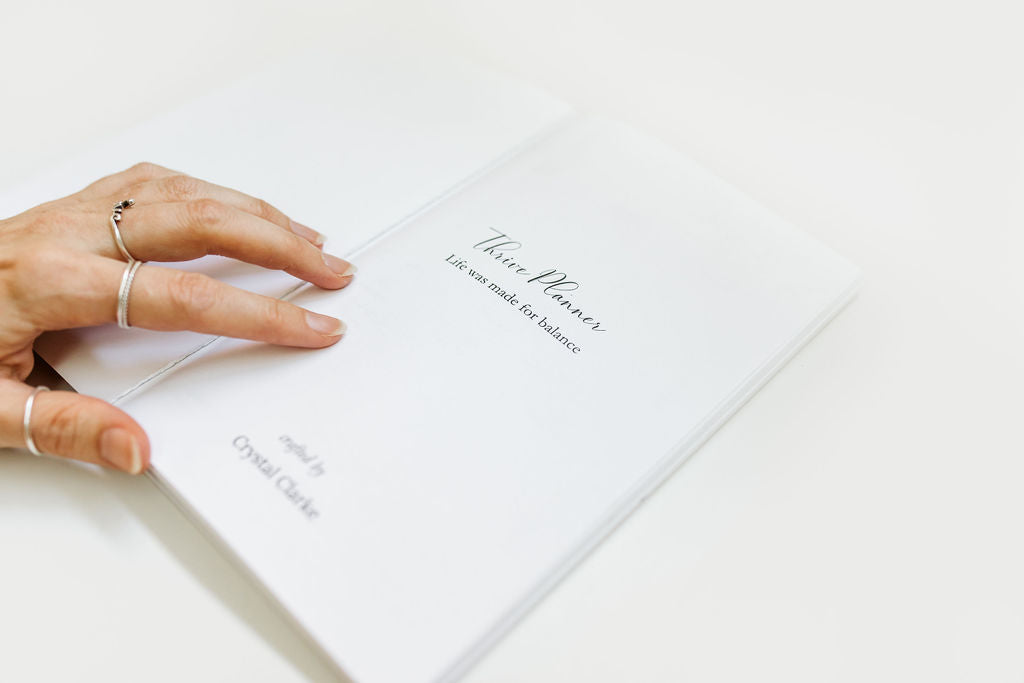 Hand holding a book titled 'Thrive Planner' on a white surface
