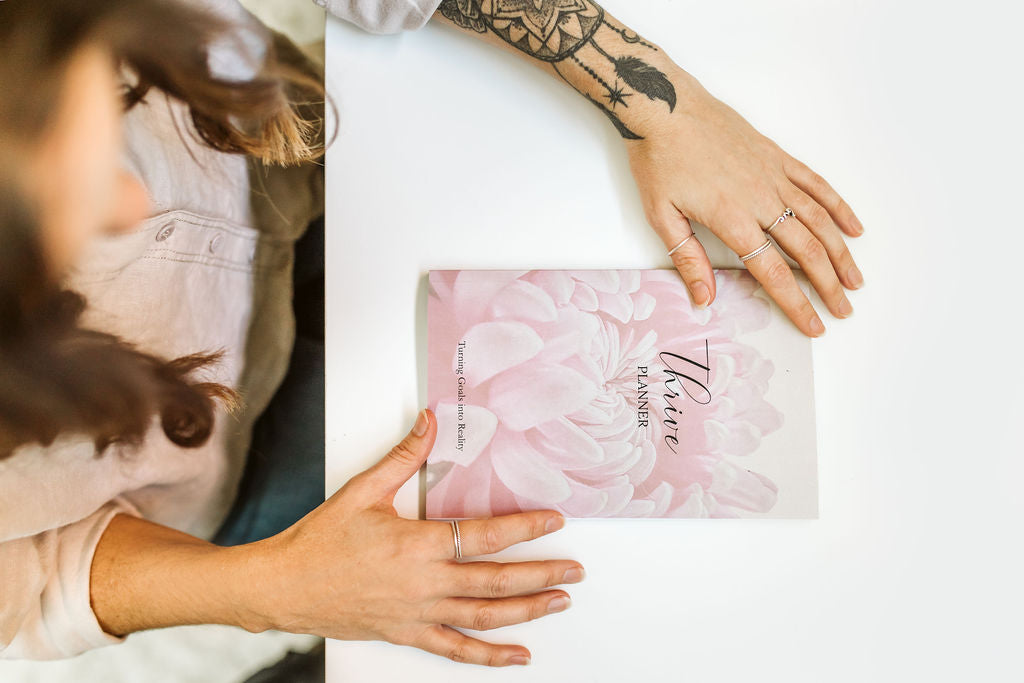 Person holding a pink floral notebook with 'Thrive' on a white background