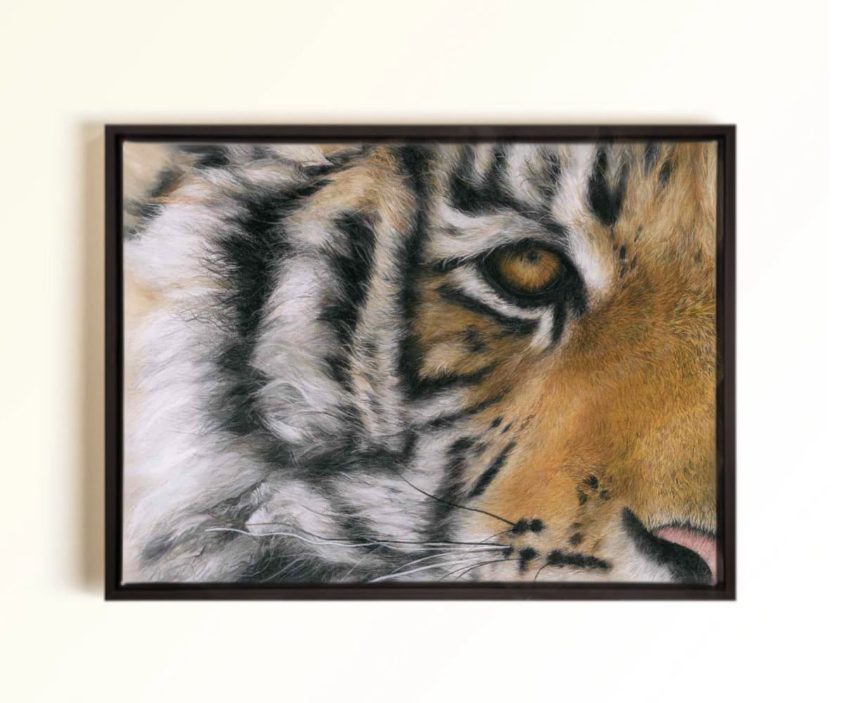 A framed close-up tiger face artwork hanging on a light beige wall. The print or painting shows the tiger's face in profile with orange, black, white, and gray fur details, enclosed in a dark frame.