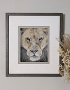 Framed portrait of a lion on a light gray wall with decorative elements.