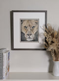 Framed artwork of a lion's face on a shelf with books and a vase.