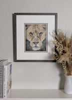 Framed artwork of a lion's face on a shelf with books and a vase.