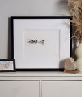 Framed artwork of ducks on a white background, displayed on a shelf with decorative items.