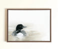 A framed pastel artwork of a loon duck floating on calm water, displayed on a light beige wall. The painting features a detailed black and white loon with gray feathers, set against a soft, misty background.
